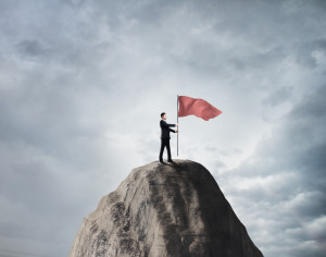 businessman standing on rock with red flag