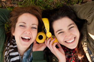 Two happy teenage girls lying on the grass sharing headphones to listen to music